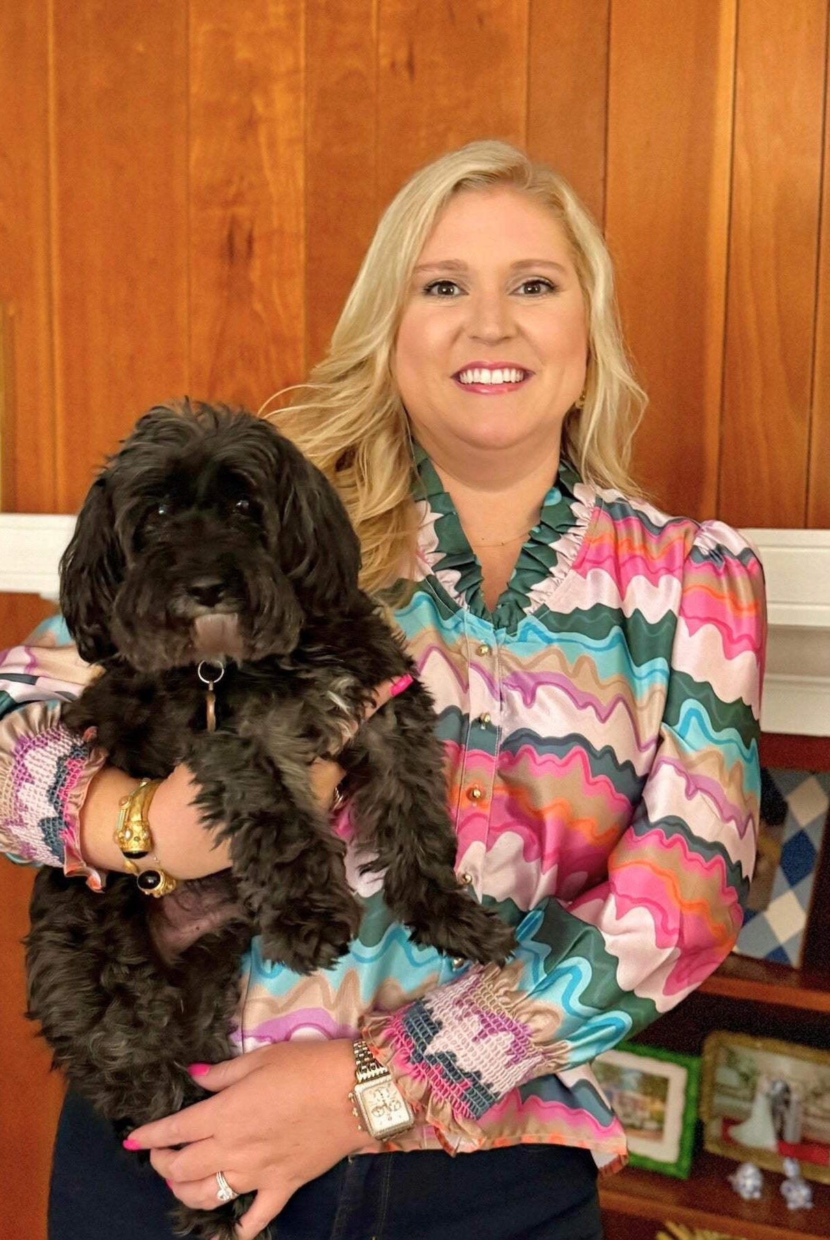 Woman wearing colorful Harper Top holding black dog in cozy indoor setting