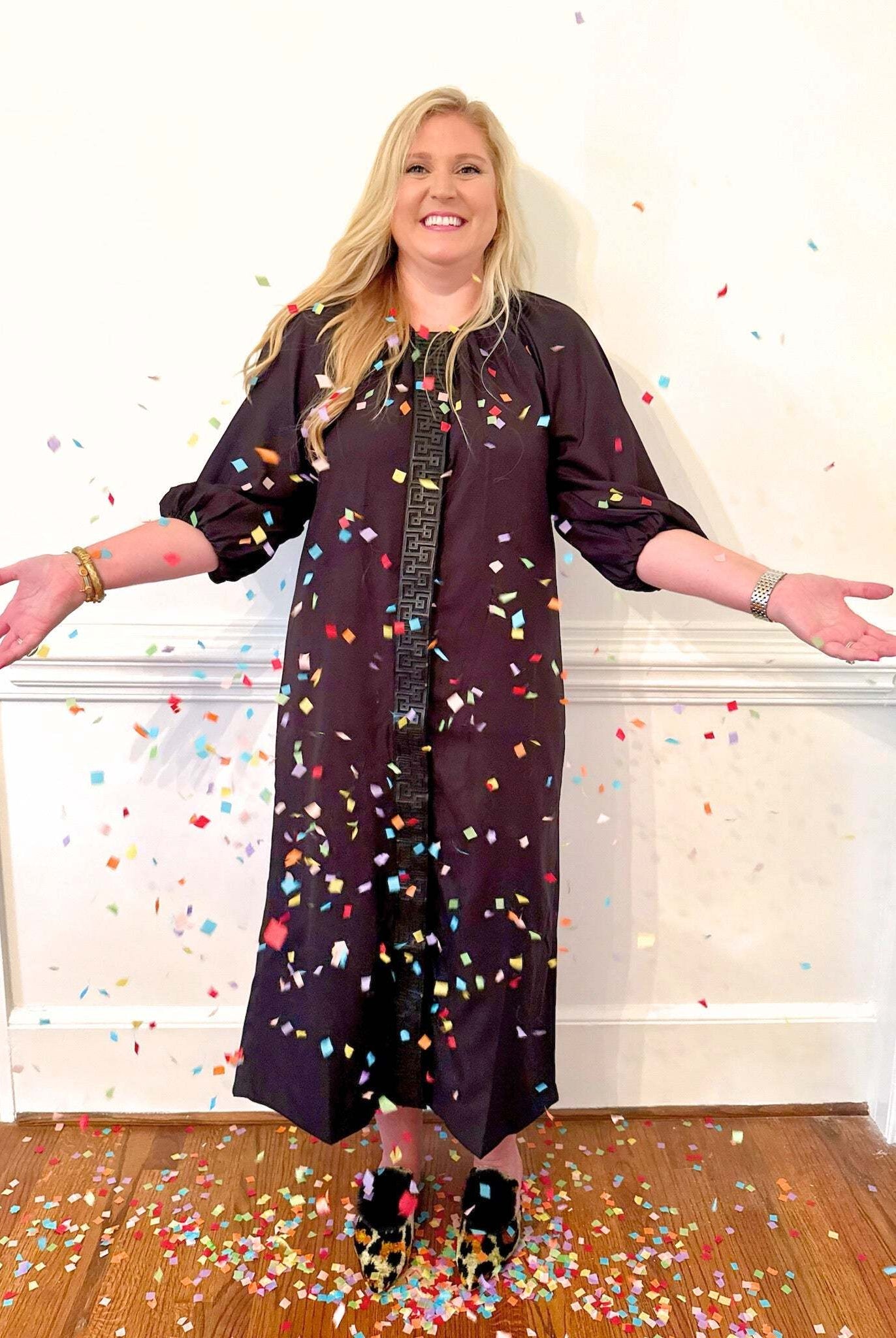 Woman wearing a black Fall Hampton Dress with leather Greek key detail, surrounded by colorful confetti indoors