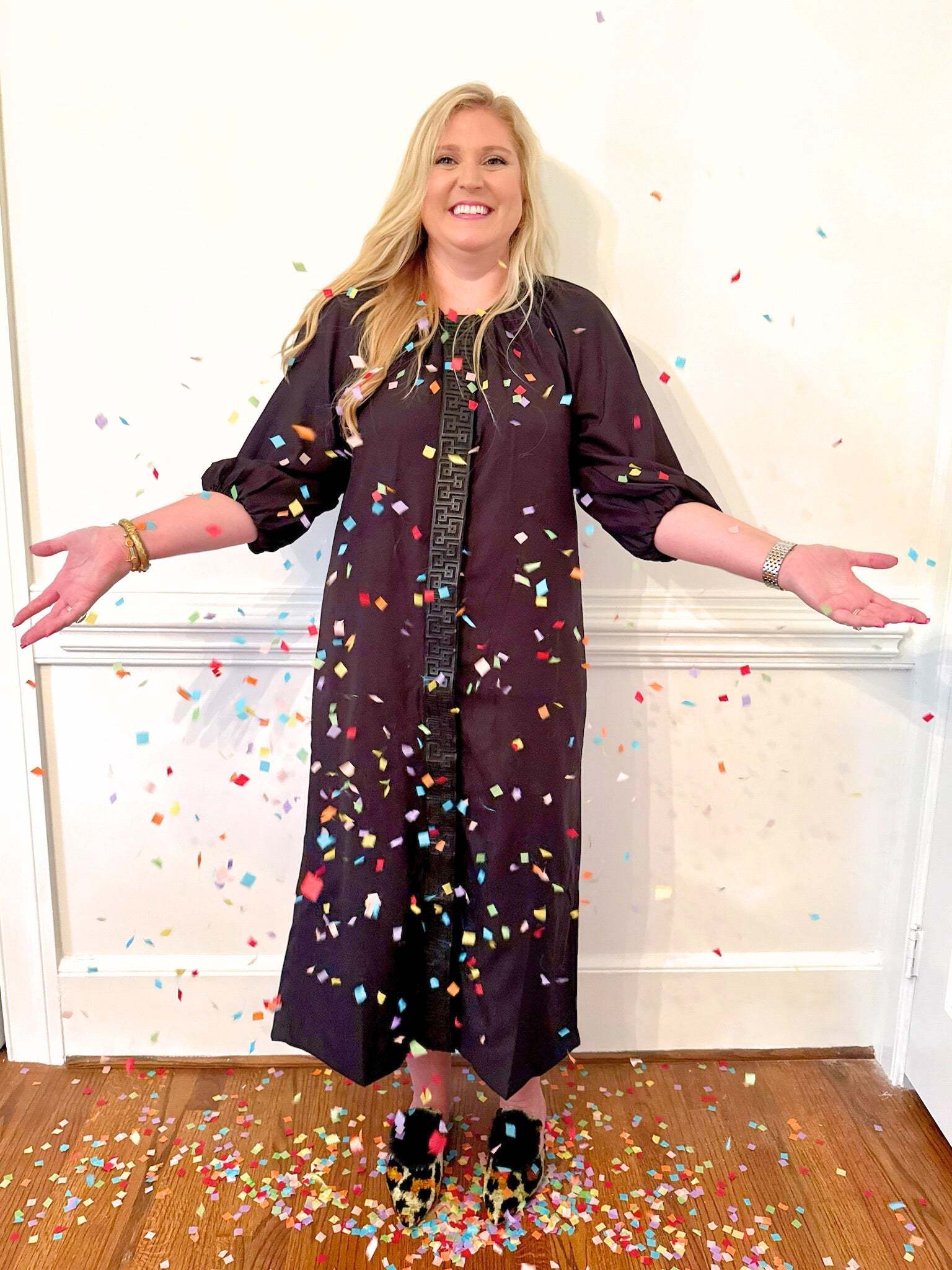 Woman wearing a black Fall Hampton Dress with leather Greek key detail, surrounded by colorful confetti indoors