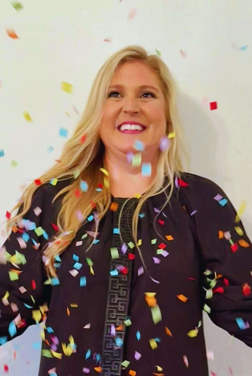 Woman wearing black Fall Hampton Dress with leather Greek key detail celebrating with colorful confetti