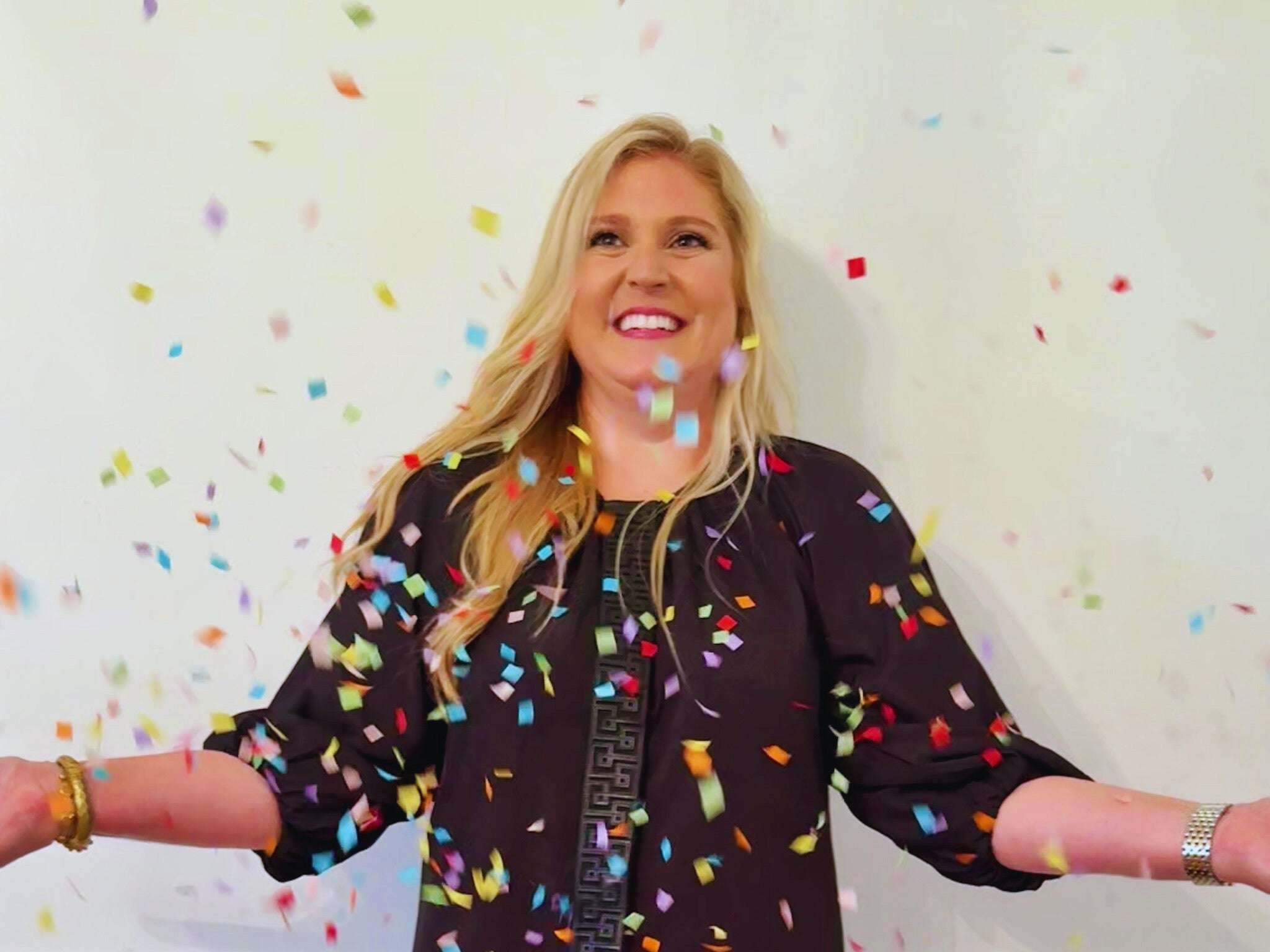 Woman wearing black Fall Hampton Dress with leather Greek key detail celebrating with colorful confetti