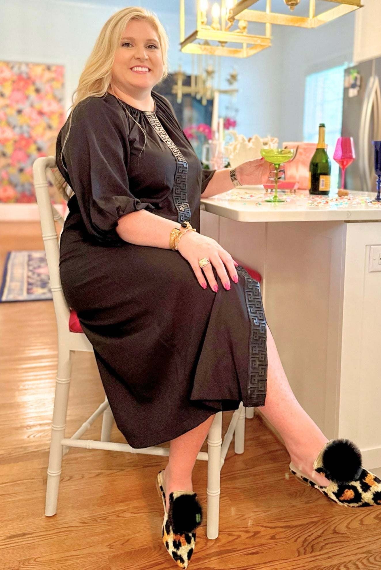 Woman wearing black Fall Hampton Dress with leather Greek key detail sitting at kitchen counter
