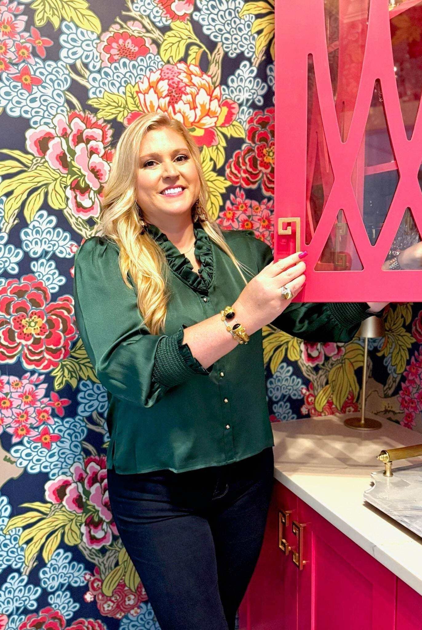 Woman wearing green Harper Top with ruffle neckline and gold buttons in colorful floral kitchen