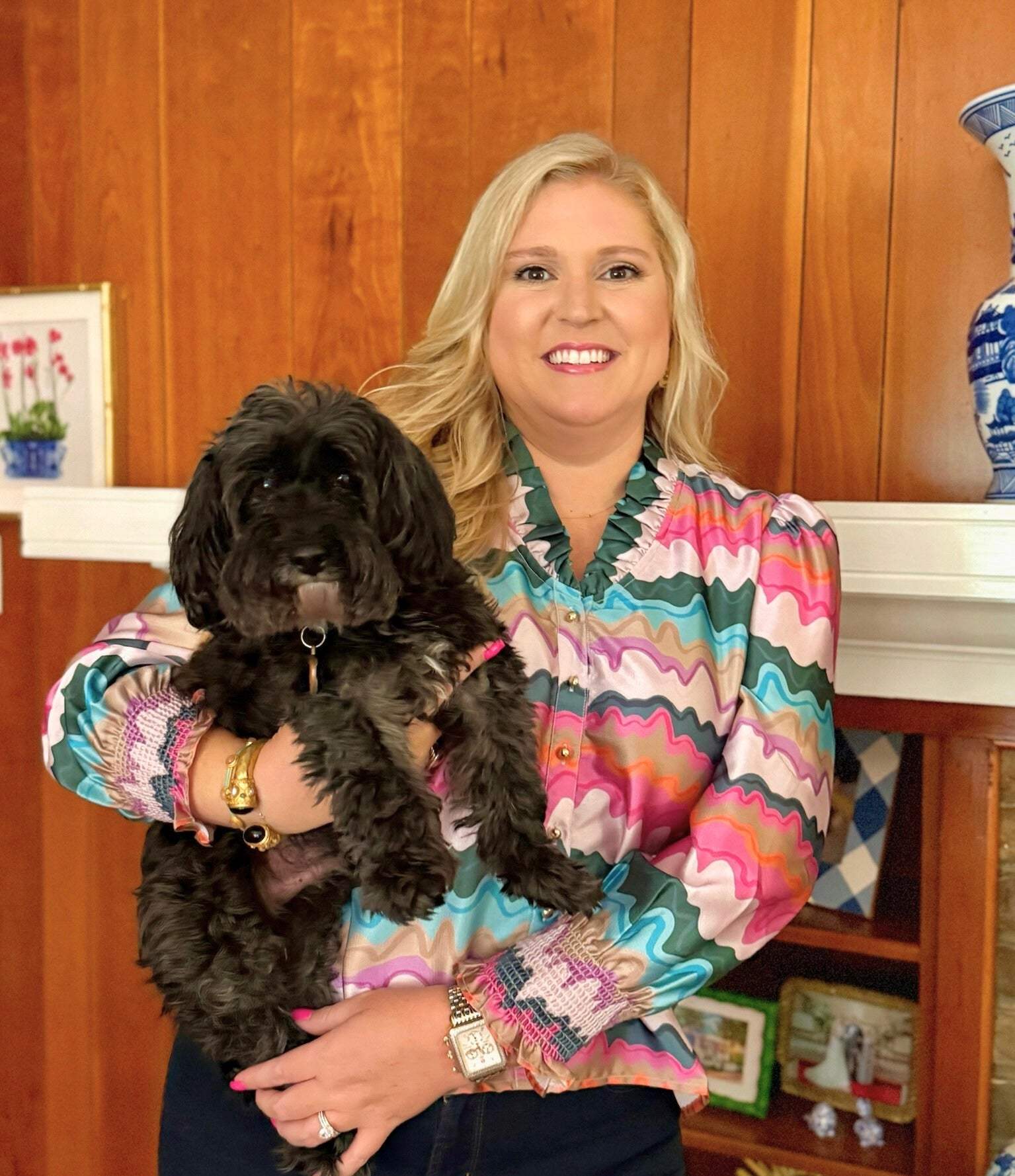 Woman wearing colorful Harper Top holding black dog in cozy indoor setting