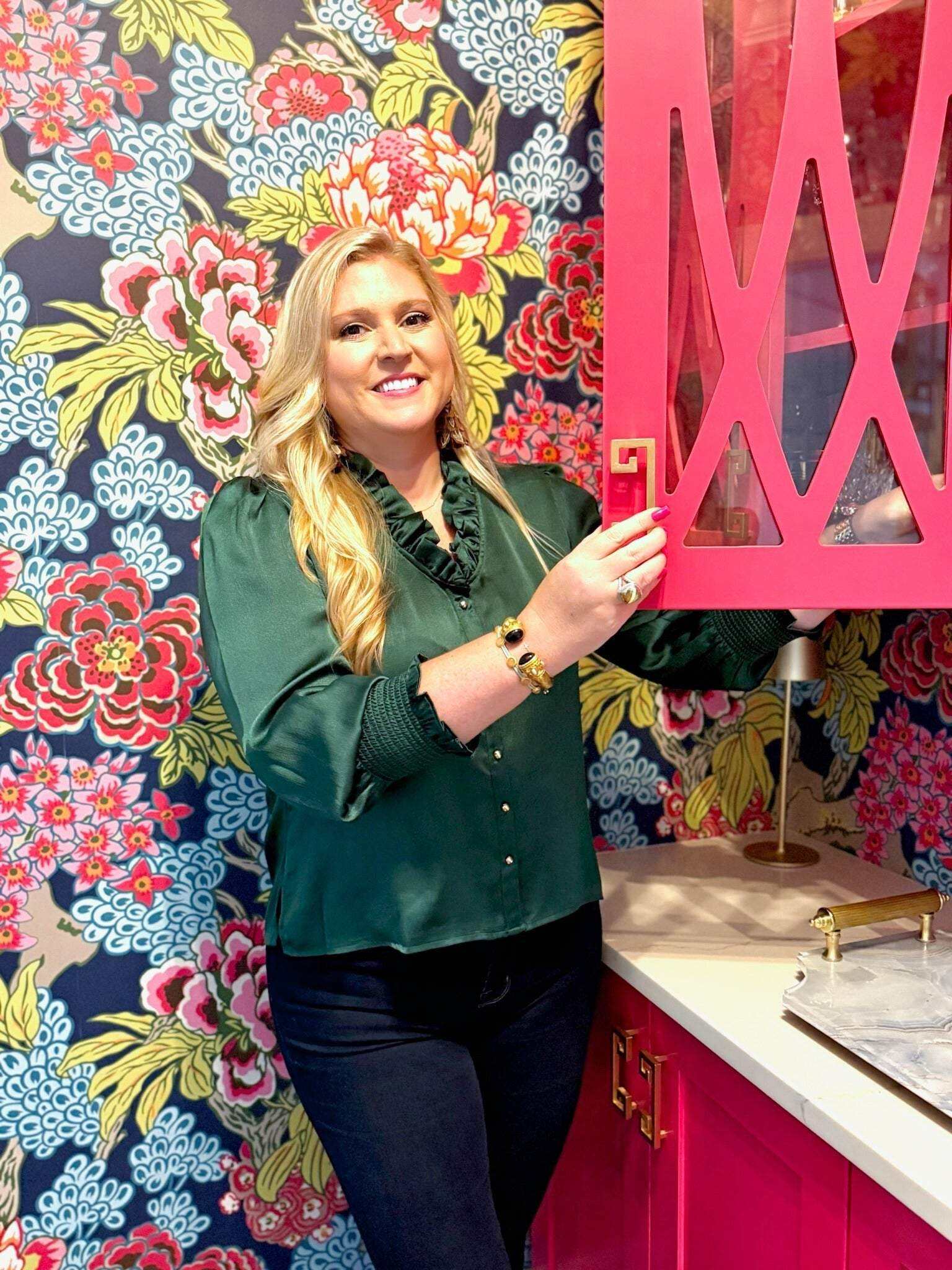 Woman wearing green Harper Top with ruffle neckline and gold buttons in colorful floral kitchen